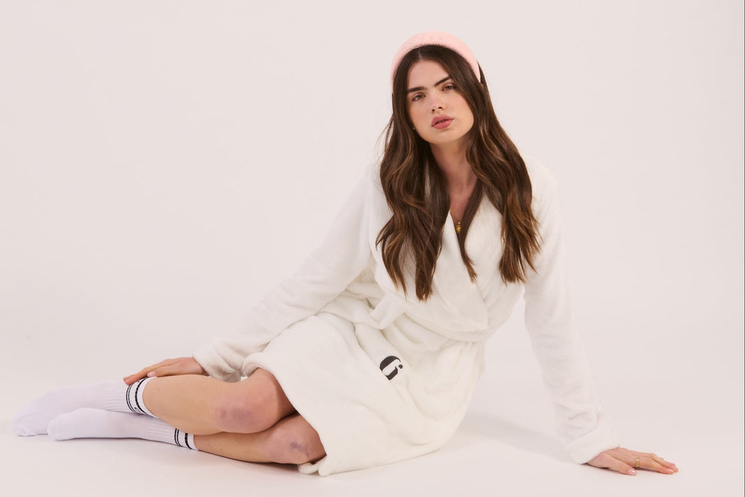 Woman wearing a white robe with a brand logo on a plain background